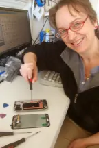 A picture of a smiling woman sitting at a desk working on a device